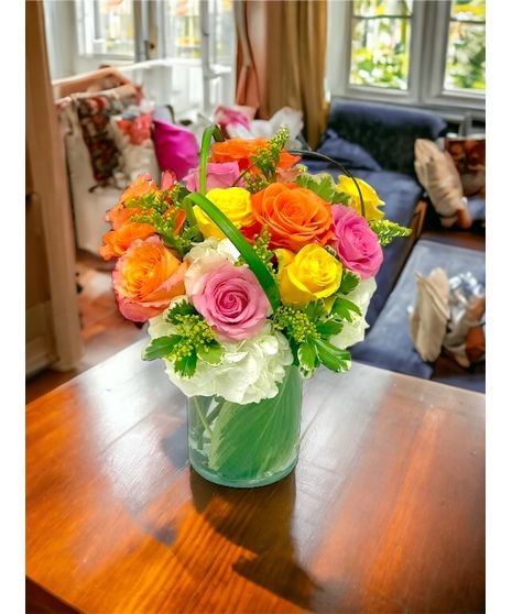 One dozen roses in assorted colors with hydrangea in a leaf lined vase.