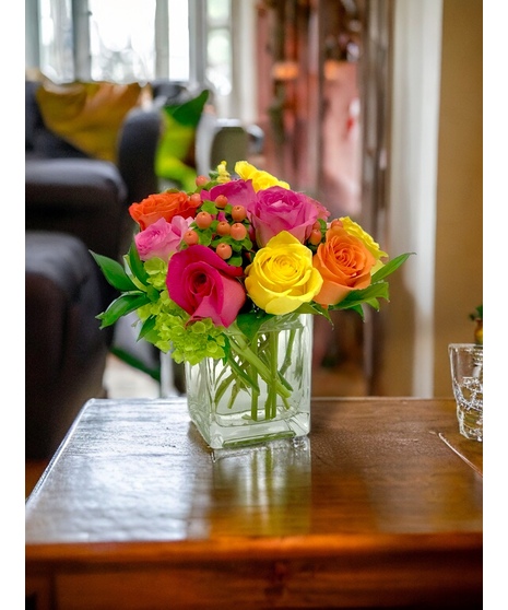 Ten brightly colored roses in a glass cube vase. 